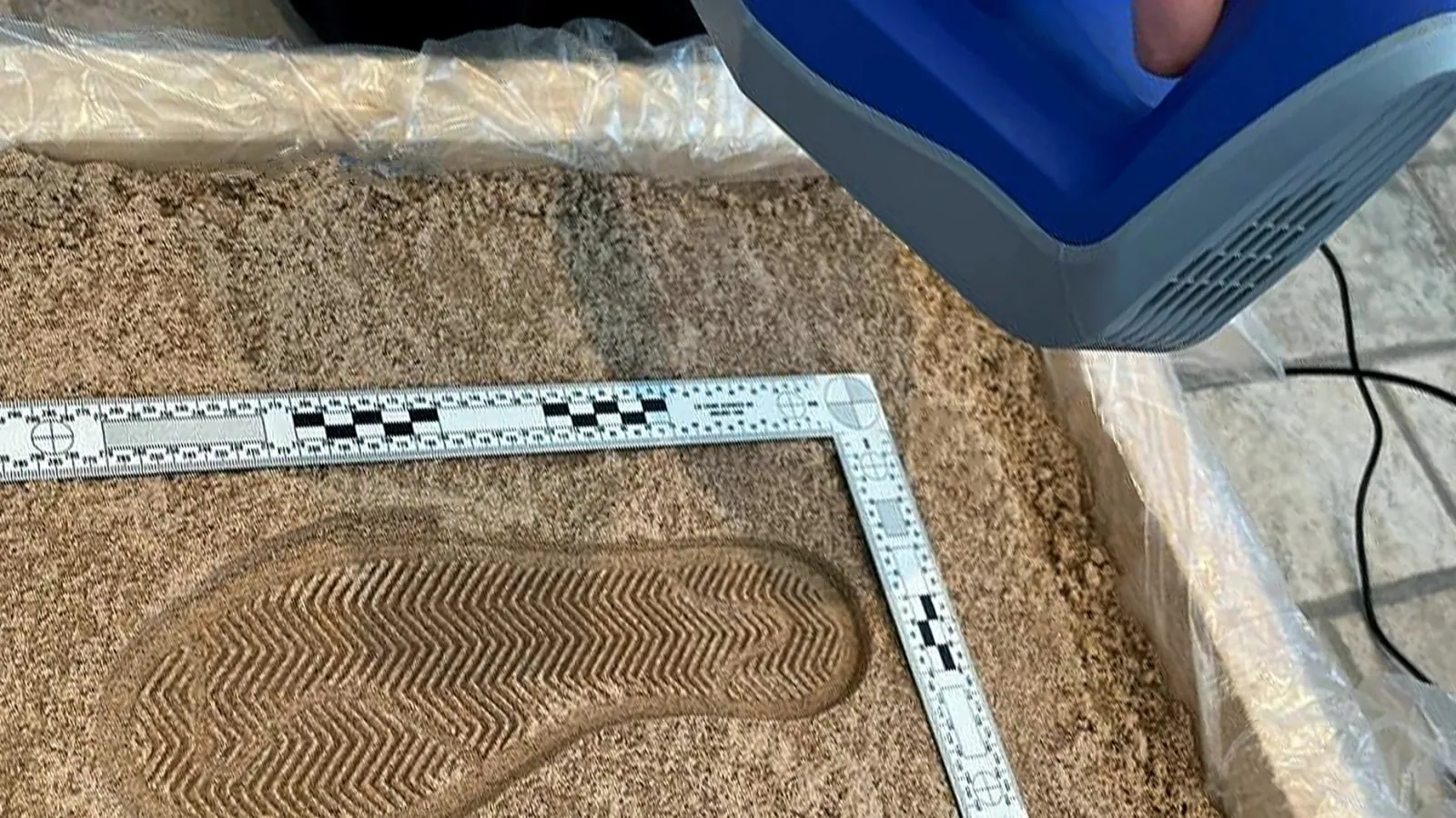 Scanner 3D Artec Space Spider di prima generazione sopra un'impronta di calzatura nella sabbia, accanto a una scala metrica forense a L