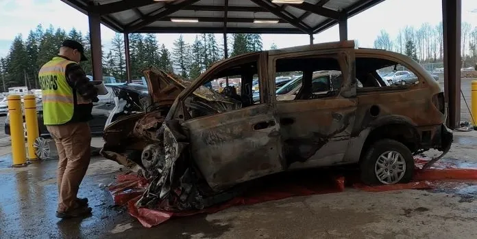 Investigator documenting a burnt-out vehicle at an accident scene