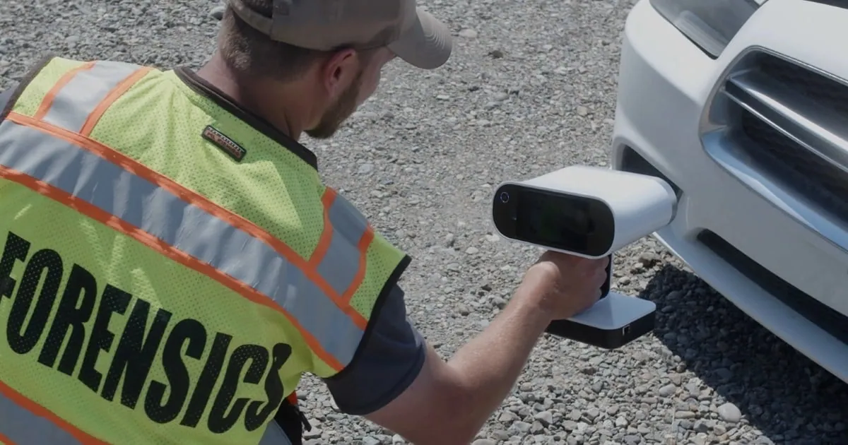 Tecnico di Origin Forensics con un gilet forense ad alta visibilità che scansiona un'auto distrutta con lo scanner 3D palmare Artec Leo